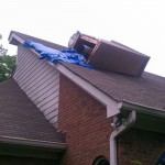 Toppled and destroyed chimney with blue tarp and flue hanging out the bottom