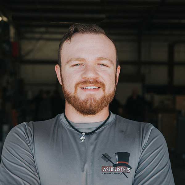 CSIA Certified chimney sweep Tim Kneller has a red beard and mustache shorter hair and a gray long sleeve with Ashbusters logo